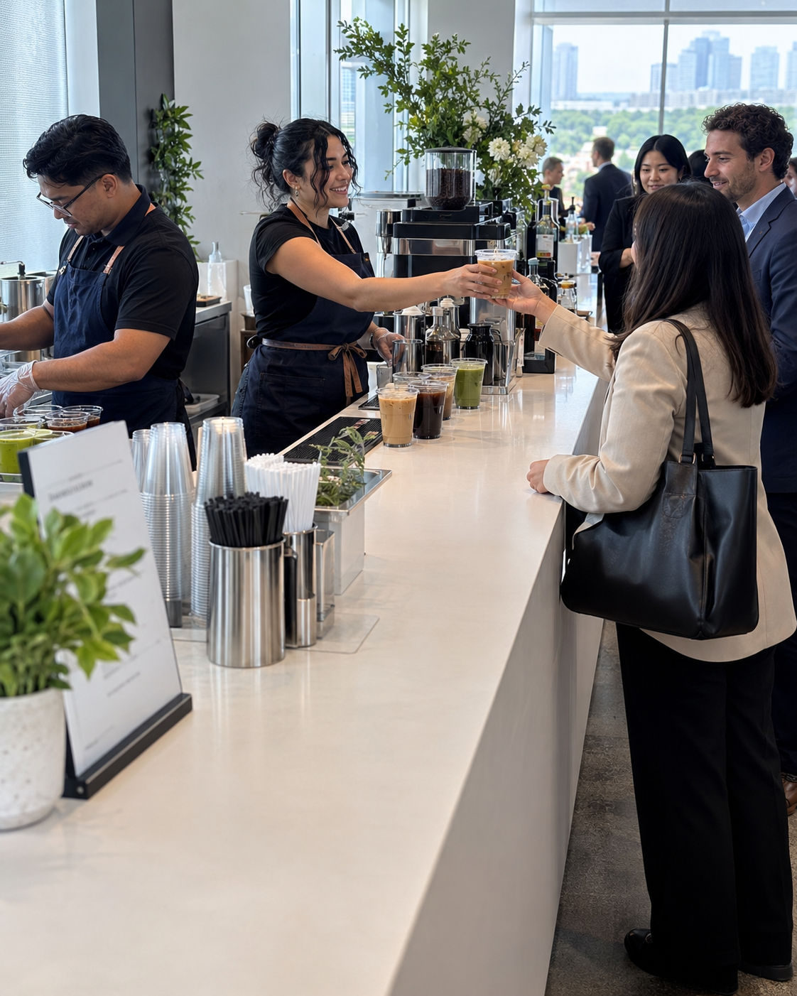 Two baristas serving guests across a white beverage bar