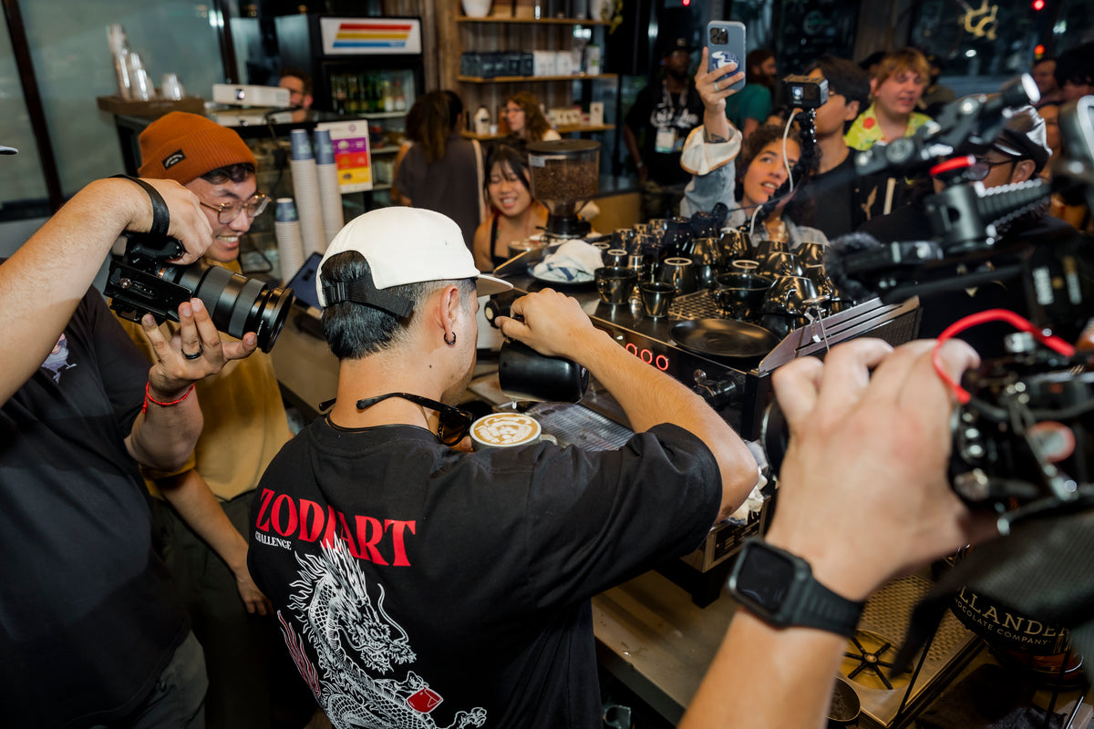 Barista pours latte art while the crowd films on phones at an ESOM throwdown in Los Angeles, 2024