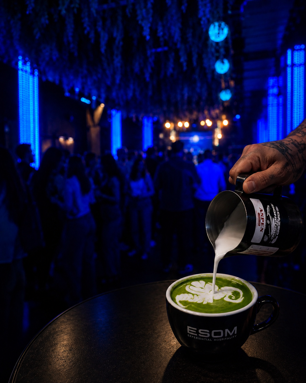 Milk poured into a matcha latte in an ESOM cup at a blue-lit evening event