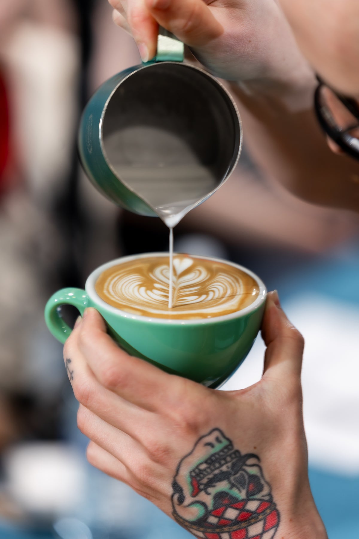 Barista pouring a rosetta into a green cup at the bar