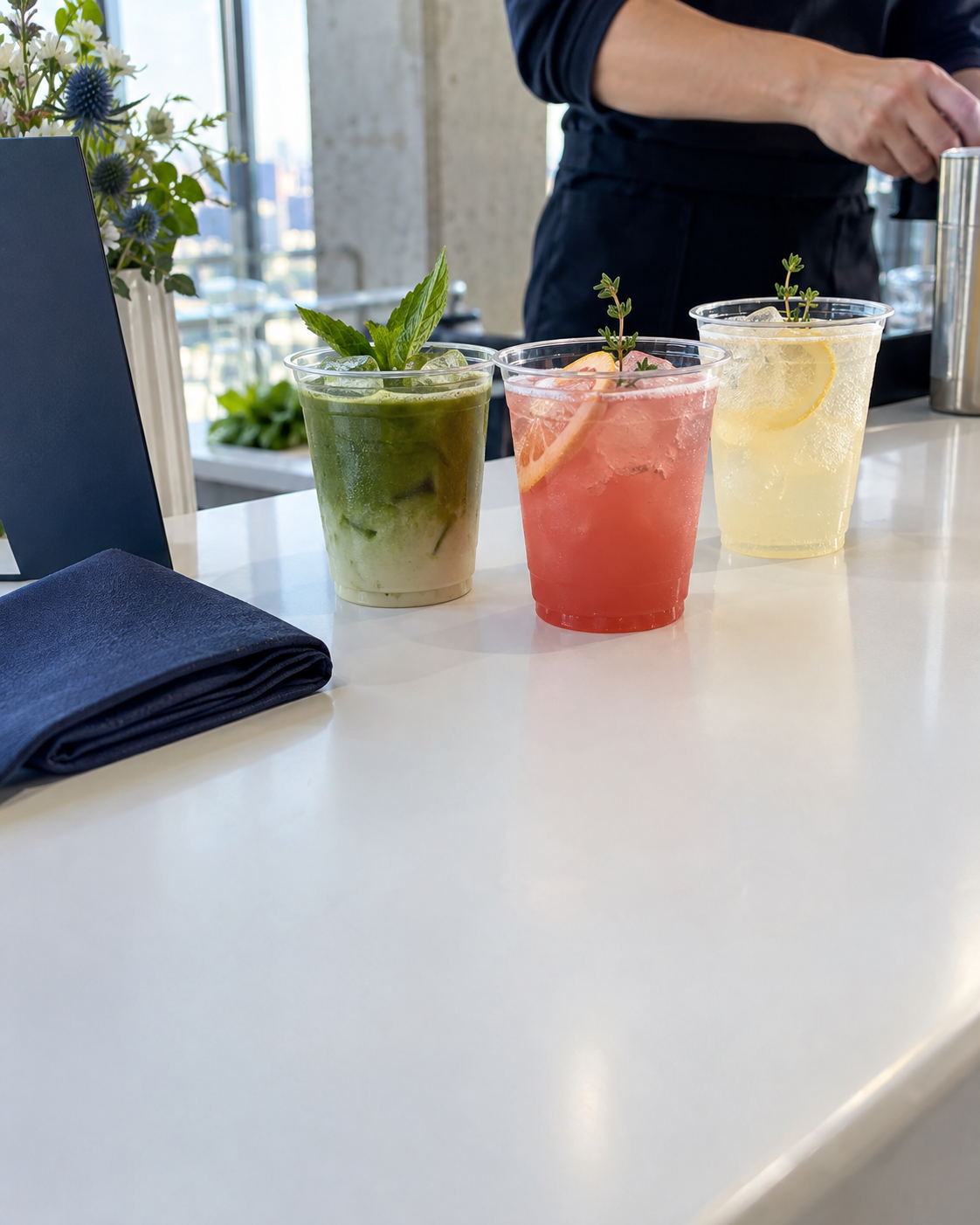 Three specialty drinks in clear cups with fresh garnishes on a white bar