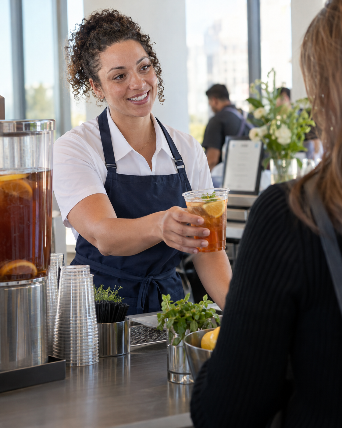 Barista in an apron handing an iced drink to a guest